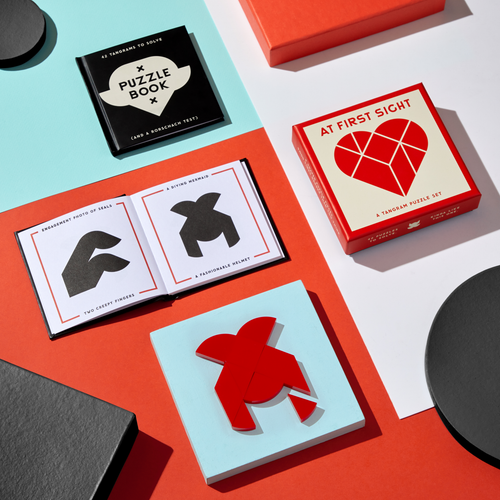 A group of boxes sits on a table, with one hiding the Brass Monkey At First Sight Tangram Puzzle—a heart-shaped, gift-ready surprise sure to delight.